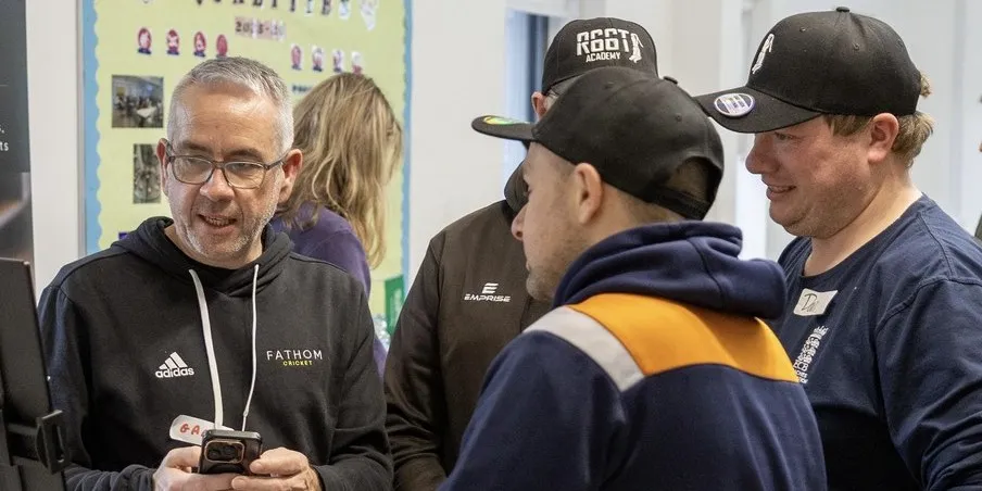 Gary Hector showing GoFathom on his phone to coaches at a stand, one wearing an R66T Academy cap